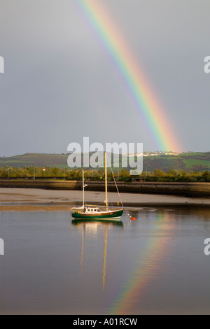 Rainbow over moored boat on river estuary with afternoon sun grey sky.  Conwy North Wales UK Stock Photo