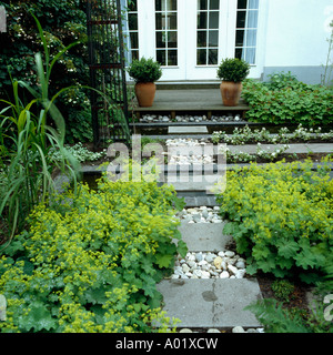 Block and peeble path to decking outside French windows small beds with lady s mantle tall grasses and a climbing hydrangea Stock Photo