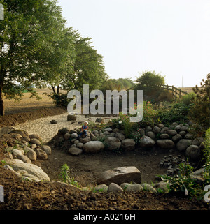 Small boy sitting on smooth boulders surrounding children's sandpit in country garden in summer Stock Photo