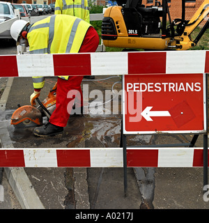 Water engineer uses a circular saw to cut through tarmac. No release required: faces cropped / masked so not recognizable. Stock Photo