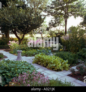 Paved path through trees formal flowering beds in summer garden Stock Photo