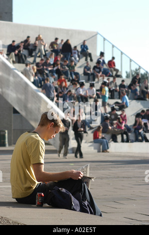 Students sitting outside in the sunshine on the La Scala  steps by Aberystwyth Arts Centre summer afternoon - man reading paper Stock Photo