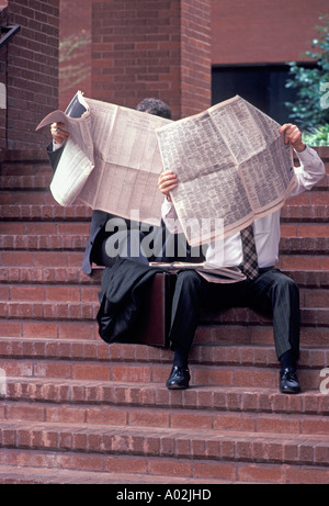 Caucasian businessmen reading newspaper on steps of office building Stock Photo