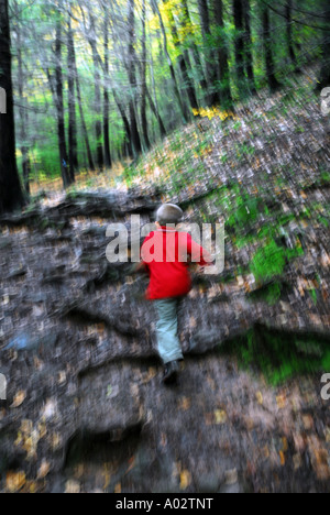 A small boy in a red shirt climbs a trail in a deep forest exploring nature or running scared Stock Photo