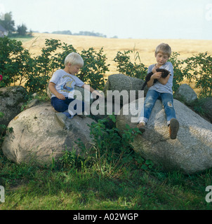 Two small boys sitting on large smooth boulders in natural country garden in summer Stock Photo