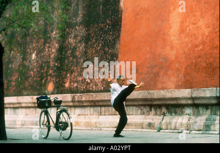 Elderly chinese man doing a high kick during early morning Tai Chi exercises next to the wall of Forbidden City Beijng China Stock Photo