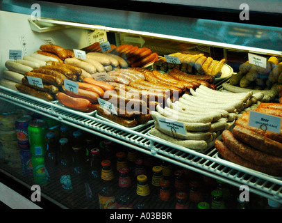 Various raw sausages for sale in a lighted glass display case above rows of soda bottles. Stock Photo