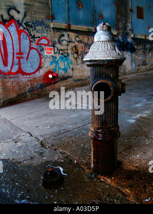 Old, open fire hydrant in front of a graffiti-covered wall near Harlem in New York City. Stock Photo