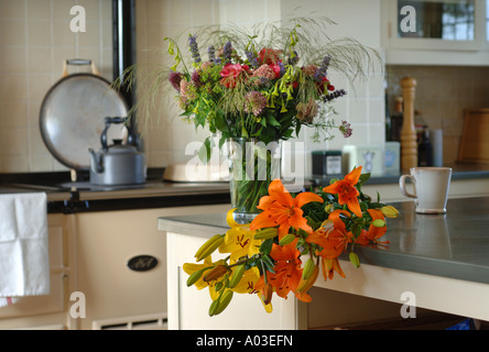 LILIES ON A COUNTRY KITCHEN TABLE WITH OTHER CUT FLOWERS IN A VASE UK Stock Photo