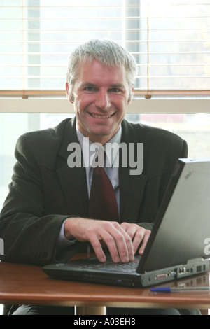 Close up of middle aged business man sitting behind his desk with a notebook computer Stock Photo