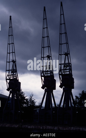 Three cranes on a building site in London's docklands silhouetted against a stormy sky London England UK Stock Photo