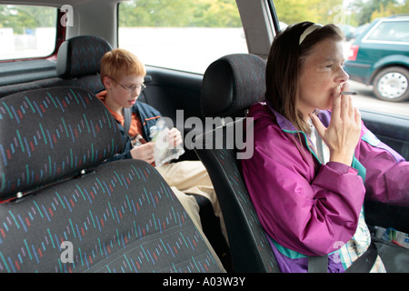 a mother smoking while driving with her small son in the back of her car Stock Photo
