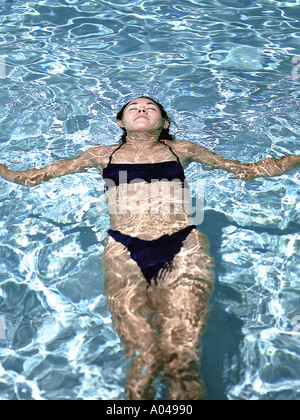 Young woman wearing black bikini floating on her back in a pool