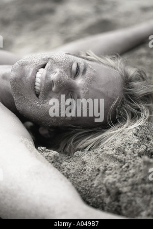 Young man smiling with arms outstretched lying on his back on the sand Stock Photo