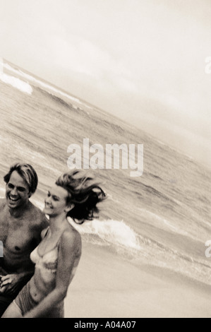 Young couple holding hands running along the beach Stock Photo