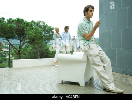 Casually dressed young executives working outdoors, man in foreground checking cell phone messages Stock Photo