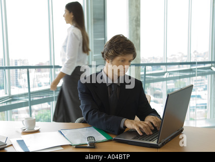 Businessman using laptop, woman walking by in background Stock Photo