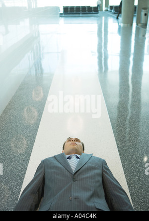 Businessman lying down on floor in airport Stock Photo