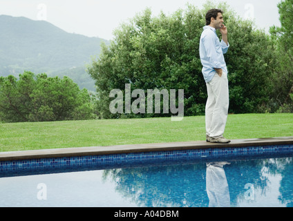 Man using cell phone by edge of pool Stock Photo