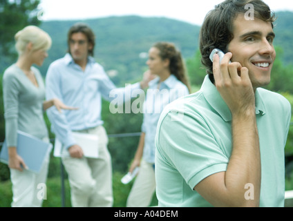 Casually dressed young executives working outdoors, man using cell phone in foreground Stock Photo