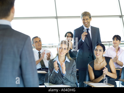 Executives in seminar, one man holding microphone, others clapping Stock Photo