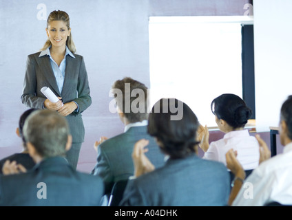 Executives sitting in seminar, woman standing facing group Stock Photo