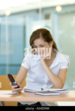 Woman sitting at desk, smiling and looking at cell phone Stock Photo