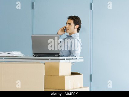 Businessman using cell phone, sitting at table top supported by cardboard boxes Stock Photo