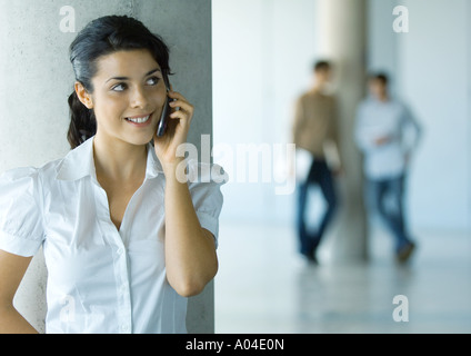 Young woman using cell phone, two men in background Stock Photo