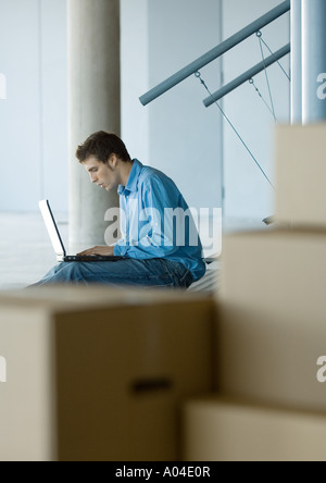 Businessman using laptop, cardboard boxes in foreground Stock Photo