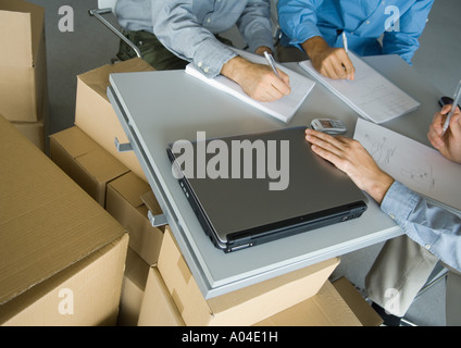 Three business men working at table, surrounded by cardboard boxes, partial view Stock Photo