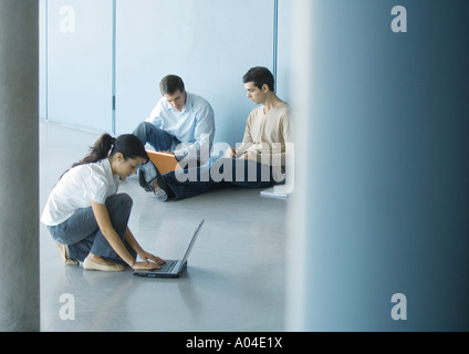 Young woman and two young men using laptops on floor Stock Photo
