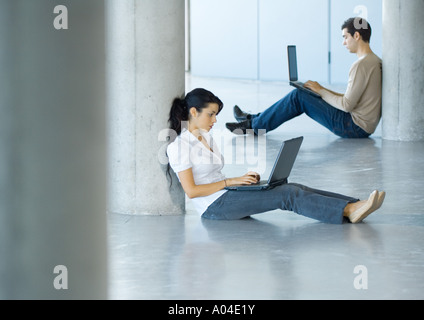 Young woman and young man sitting on floor, using laptops Stock Photo