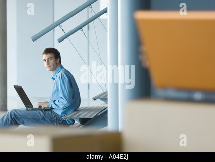 Young businessman using laptop, cardboard boxes in foreground Stock Photo