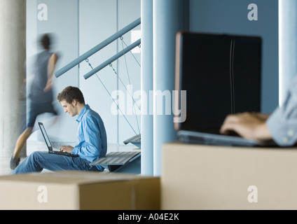 Businessman using laptop, second person using laptop on cardboard box in blurred foreground Stock Photo