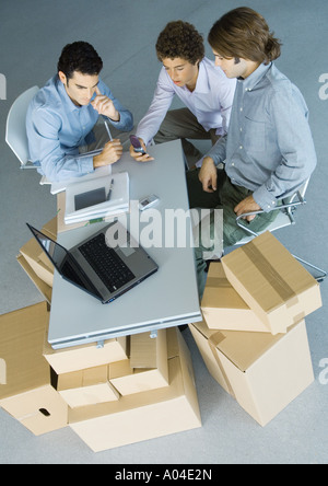 Businessmen sitting at table top supported by cardboard boxes, high angle view Stock Photo