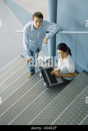 Young business professionals posing on stairs, woman sitting with laptop computer