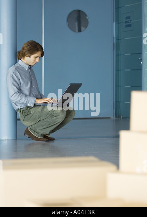 Businessman leaning against pole, using laptop, cardboard boxes in foreground Stock Photo