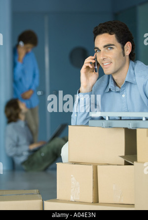 Young businessman using cellphone, sitting at table supported by cardboard boxes Stock Photo