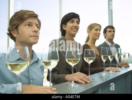 Four adults standing in row with hands on bar, glasses of wine in front of them Stock Photo