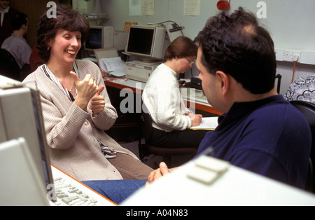 Deaf teacher working with hearing impaired adult students on computers. Stock Photo