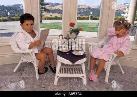 little man reading paper with little lady in robe and slippers crying while having their morning breakfast and tea Stock Photo