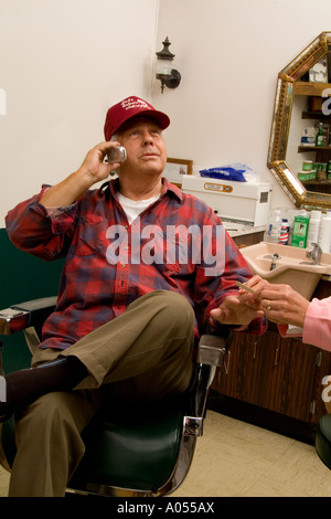 Small middle town barber shop in America trucker type man getting a manicure while talking on cell phone odd situation humorous Stock Photo