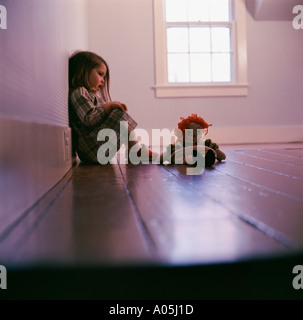 Little girl sitting in the corner of an empty room with her Raggedy Ann doll looking sad Stock Photo