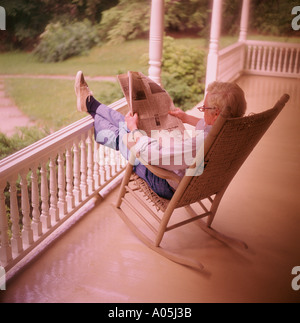 Mature white hair man sitting on a rocking chair on the front porch reading the newspaper Stock Photo