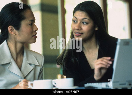 An Asian and Latino woman having a business meeting drinking coffee in front of their laptops Stock Photo