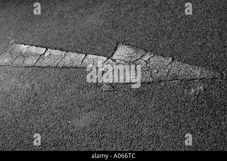 An arrow is painted on the road with cracks on it Stock Photo