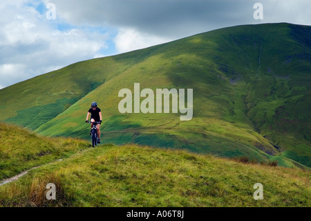 Female mountain biker on a track on Bluecaster Side in Cumbria with the Howgill Fells behind Stock Photo