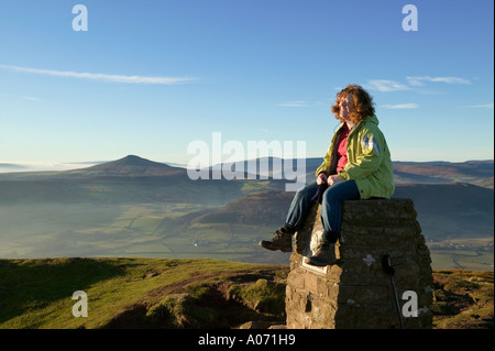 Female hiker laughing while sitting on the trig point Skirrid Fawr Wales UK Stock Photo