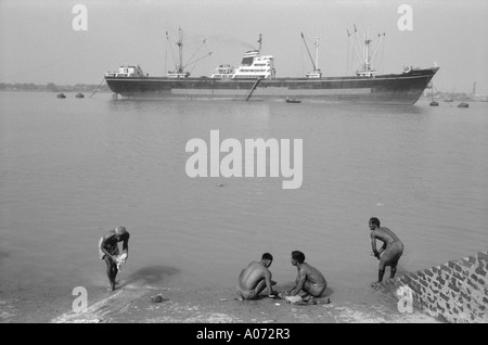 Four men washing clothes and ship in Hoogly river Calcutta Kolkata West Bengal India Stock Photo